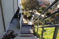 Plattformlift an einer steilen Außentreppe neben einem Einfamilienhaus, der einen barrierefreien Weg vom Garten- und Straßenbereich zum Hauseingang ermöglicht.