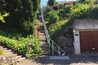 Lange Treppenanlage in Hanglage mit seitlich montierter Führungsschiene für einen Plattformlift, die vom Parkplatz hinauf zum Haus durch den Garten führt.