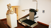 Platformlift X3 in a museum next to a sculpture and straight stairs
